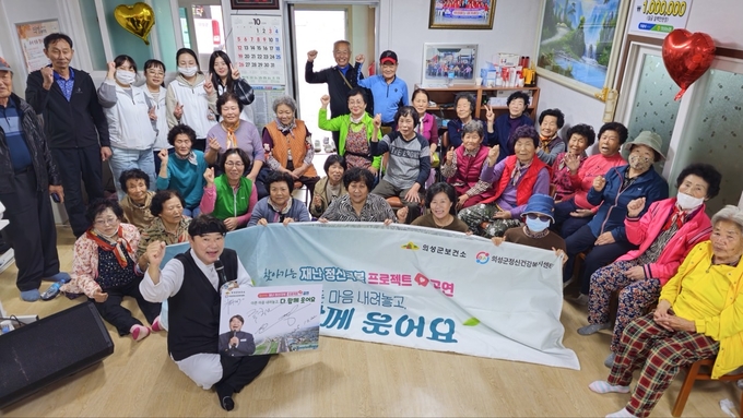 ▲ 의성군 정신건강복지센터와 방송인 한기웅 씨가 22일 의성군 철파리 마을회관에서 ‘찾아가는 재난 정신극복 프로젝트’ 공연을 열고 주민들과 함께 손을 들어 화이팅을 외치며 심리회복 메시지를 전하고 있다. 의성군