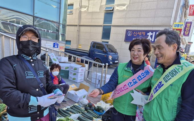 ▲ 27일 공설시장 한 상인이 한세현 회장과 전호란 부녀회장이 나눠주는 장바구니를 받고 기뻐하고 있다. 권오석 기자