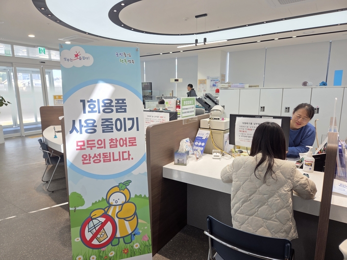 ▲ 성주읍행정복지센터 민원실에 설치된 ‘1회용품 사용 줄이기’ 안내 배너 앞에서 주민이 친환경 보상교환사업에 참여하고 있다. 성주읍은 일회용품 수거를 통한 자원 절약과 환경 보호 실천운동을 지속적으로 추진 중이다. 성주읍