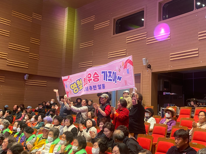 ▲ 3일 저녁 의성군청소년문화의집 공연장에서 열린 ‘의성읍민 작은음악회’에서 객석의 주민들이 ‘영철 최우승 가즈아’라고 적힌 현수막을 흔들며 함성과 박수로 응원하고 있다. 의성군