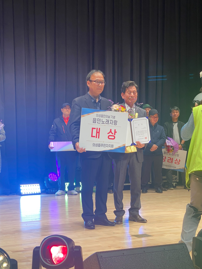 ▲ 3일 의성읍민의 날 기념 ‘의성읍민 작은음악회’ 시상식에서 업1리 배영철 씨가 ‘진또배기’로 대상을 수상한 뒤 권정일 의성읍장과 함께 상장과 꽃다발을 들고 기념촬영을 하고 있다. 의성군