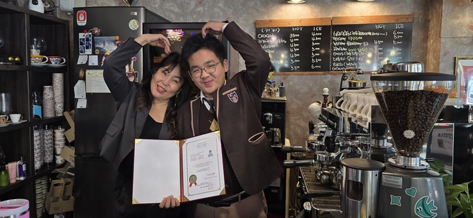 ▲ 바리스타 2급 자격증을 취득한 남 군(사진 오른쪽)이 지도를 맡은 윤미영 청송커피엠버 대표와 손하트를 그리고 있다.
