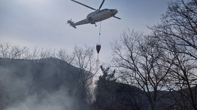 ▲ 3월 의성군 산불 현장에서 산림청 진화헬기가 연기 피어오르는 산등성 상공에서 버킷을 이용해 직접 살수를 실시하며 확산 저지에 나선 모습. 의성군
