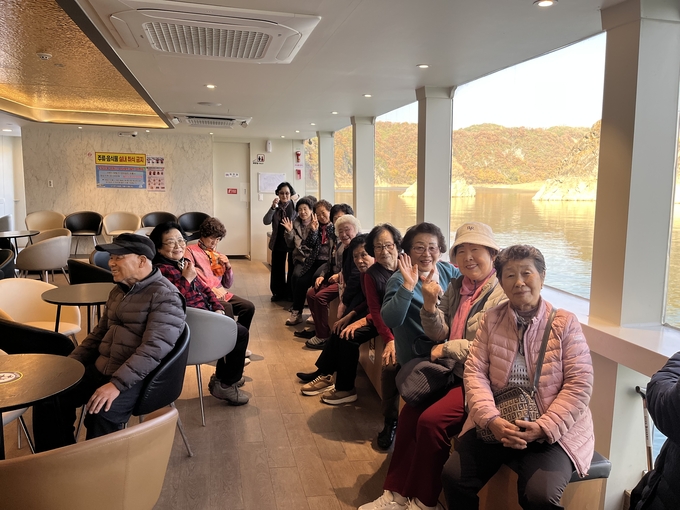▲ 의성노인복지관 어르신들이 지난 12일 단양 도담삼봉 유람선 내부에서 가을 단풍과 강 풍경을 바라보며 밝게 손을 흔들고 있다. 의성노인복지관