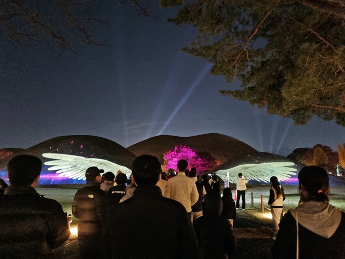 ▲ 지난달 24일부터 대릉원 일원에서 열린 ‘2025 국가유산 미디어아트 경주 대릉원’ 행사에서 관람객들이 고분에 투사된 미디어아트 영상을 감상하고 있다. 경주시