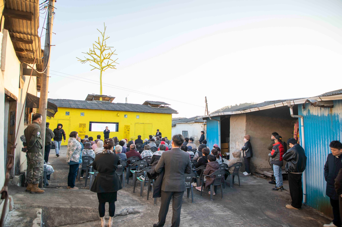 ▲ 18일 오후 의성성냥공장 마당에서 김진우 작가가 주민 100여 명에게 전시 취지를 설명하는 가운데, 노란색 외벽과 거대한 설치작품 ‘성냥나무’가 해 질 녘 하늘을 배경으로 드러나 산업유산 재생 현장의 분위기를 생생하게 보여주고 있다. 이정환 감독(포토그레퍼)