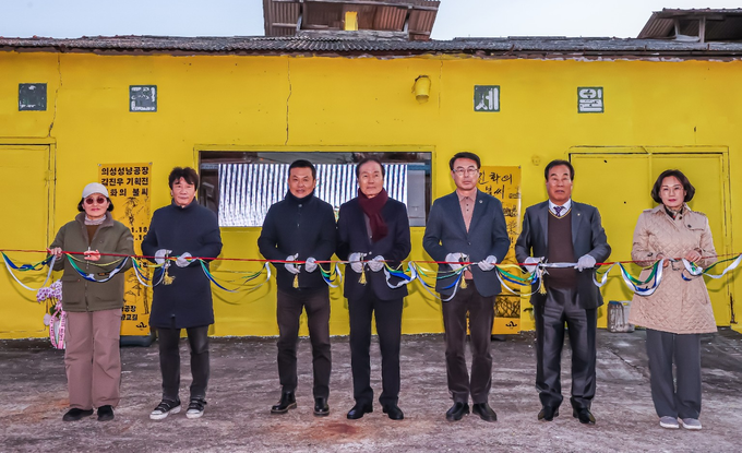 ▲ 18일 의성성냥공장 기획전 개막식에서 김진우 작가(왼쪽 세 번째부터)를 비롯해 김주수 의성군수, 이충원 경북도의원, 박태주 의성문화원장 등이 노란 외벽을 배경으로 일렬에 서서 장갑을 착용한 채 여러 색 리본을 함께 잡아 들어 올리며 개막 퍼포먼스를 진행하는 장면이 차가운 날씨 속에서도 활기 있게 펼쳐졌다. 의성군