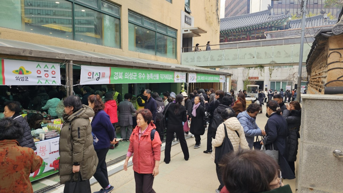 ▲ 21일 서울 종로구 조계사 인근에서 열린 의성군 우수 농특산물 직거래장터에 시민들이 마늘·사과·버섯·장류 등 지역 농특산물이 빼곡히 진열된 판매대를 둘러싸며 발걸음을 멈추고 상품을 고르는 장면이 장날처럼 붐비는 분위기로 연출됐다. 의성군