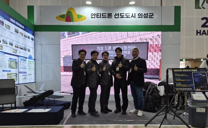 ▲ 11월 18일 청주 오스코에서 열린 ‘2025 대한민국 대드론 박람회’ 의성군 홍보관에서 강구현 신공항지원과 항공미래산업팀장(왼쪽부터), 오경호 안티드론추진단장, 김희대 신공항지원과장, 최영재 의성군 홍보대사, 송민용 일루모어 대표가 안티드론 산업지원센터 조성과 국가 안티드론 훈련장 운영 계획을 소개한 뒤 함께 기념촬영을 하고 있다. 의성군