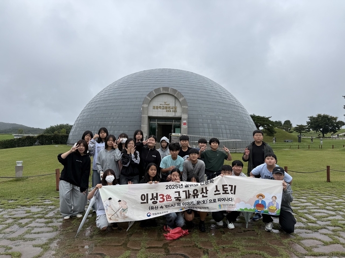 ▲ 약 8개월간 우리 고장을 직접 탐방한 활동의 일환으로 의성초 6학년 학생들이 조문국박물관 야외 전시관 앞 잔디광장에서 단체 현수막을 들고 모여 서 있으며, 흐린 날씨 속에서도 각자 포즈를 취하며 탐험 프로그램 참여 성취를 기록하는 모습이다. 경상북도의성교육지원청